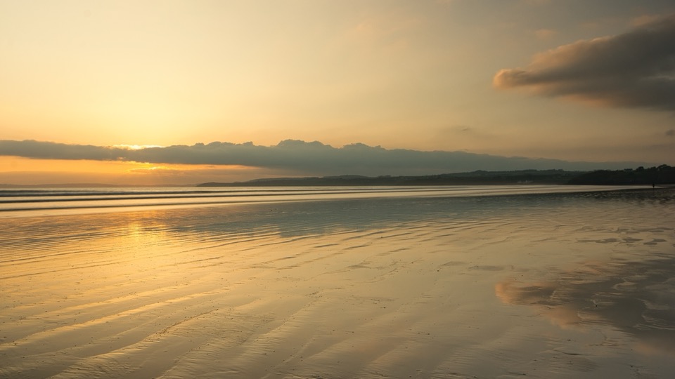 Sonnenuntergang über dem Strand von Saint-Nic, orangefarbener Himmel spiegelt sich im nassen Sand