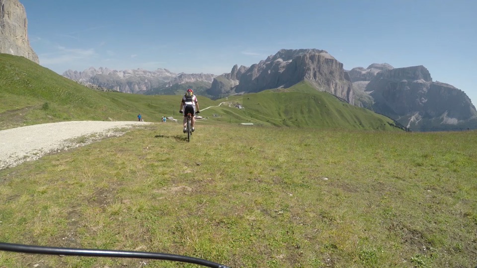 Mountainbiker fährt über eine Almwiese auf die Dolomiten zu