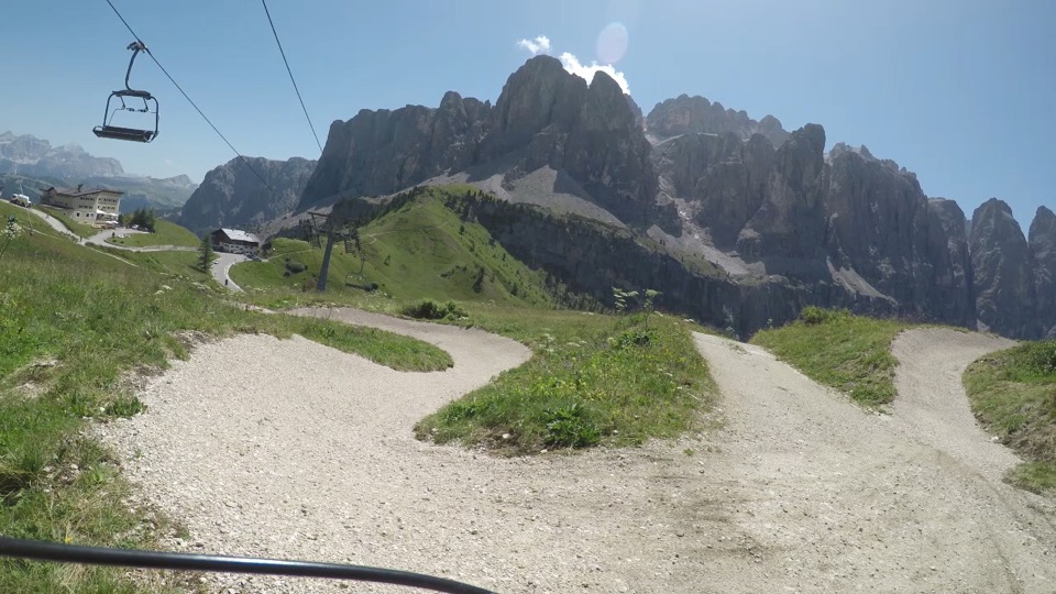 Blick vom Mountainbike auf verschlungene Schotterwege vor dem Sella-Massiv, Sessellift im Vordergrund