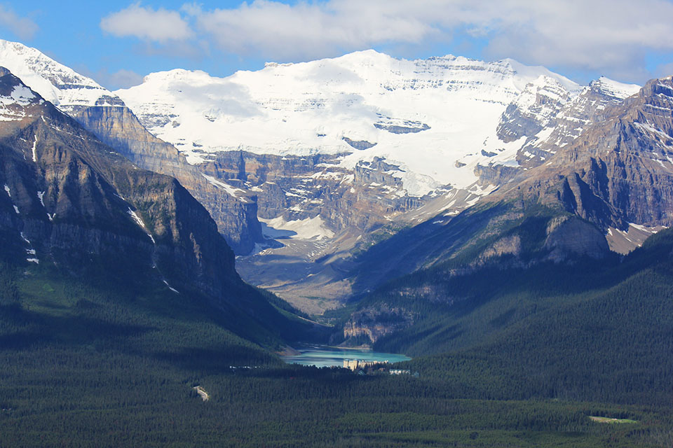 Blick von oben auf das türkisfarbene Lake Louise, eingerahmt von schneebedeckten Gipfeln und einem Gletscher