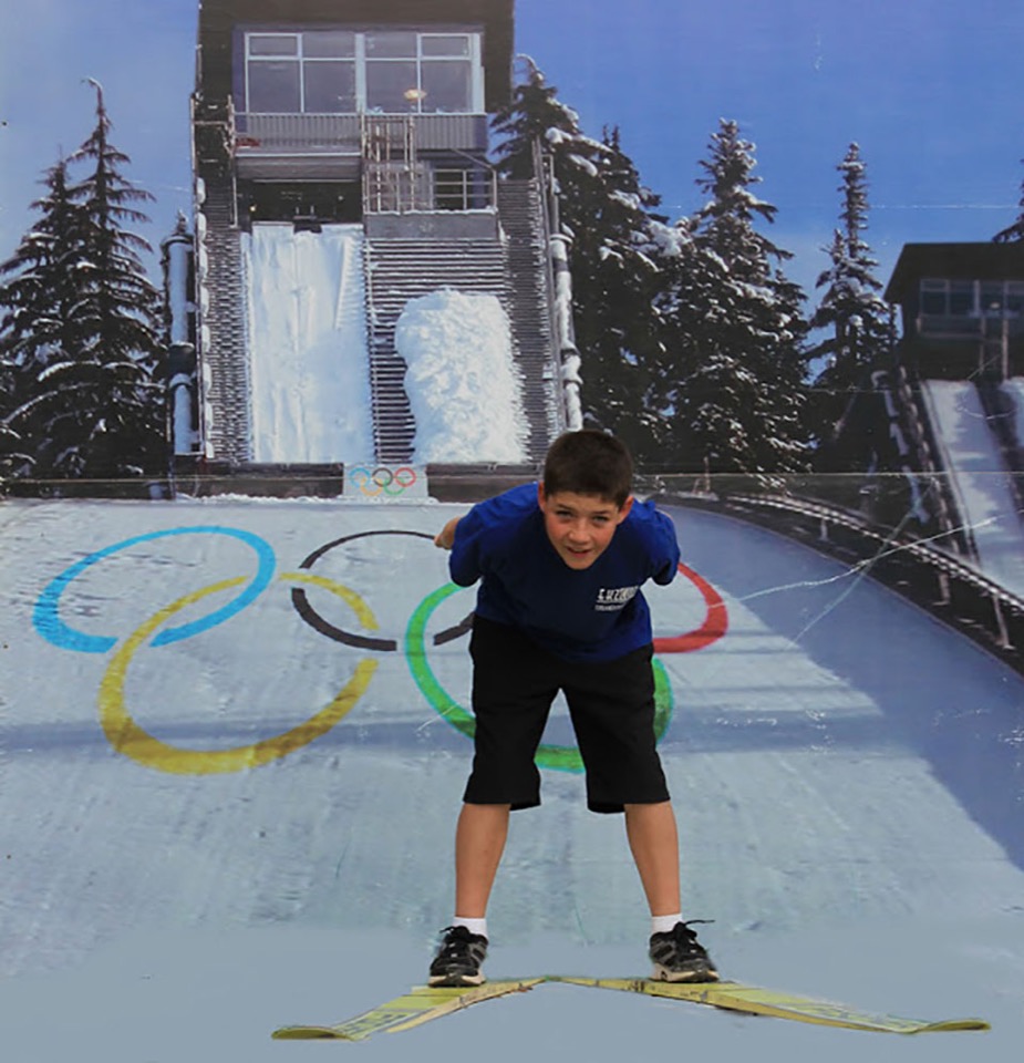 Junge posiert vor einer Fotokulisse der Skisprungschanze von Whistler