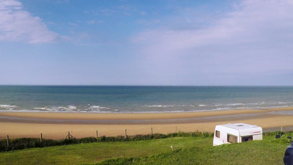 Weiter Sandstrand von Omaha Beach mit Camper am Klippenrand, aufgenommen bei einlaufender Flut