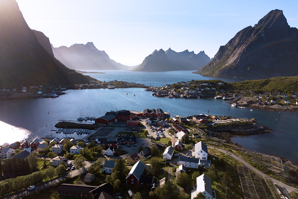 Luftaufnahme des Fischerdorfs Reine auf den Lofoten, umgeben von steilen Gipfeln und einem türkisblauen Fjord