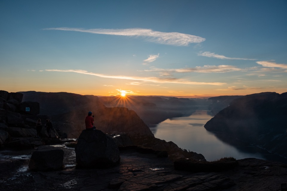 Person sitzt bei Sonnenaufgang auf einem Felsen und blickt über den Lysefjord