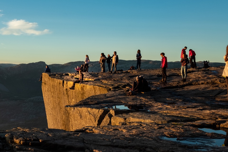 Besucherinnen und Besucher stehen im goldenen Morgenlicht auf dem Plateau des Preikestolen