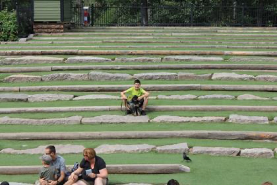 Familie sitzt mit Hund auf den steinernen Sitzstufen des Freilufttheaters in Astrid Lindgrens Welt