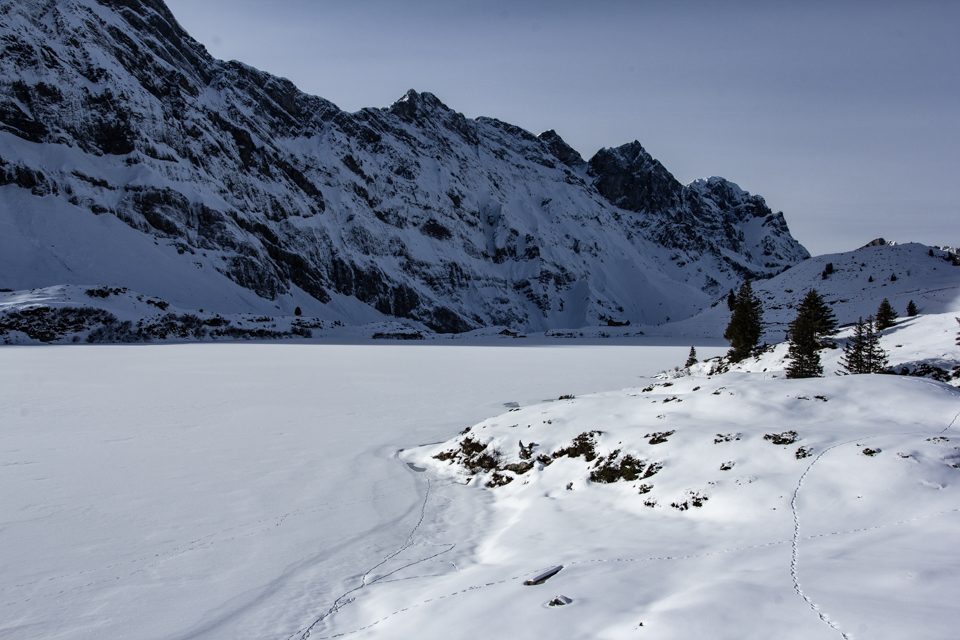 Zugefrorener Bergsee beim Trübsee, umgeben von schneebedeckten Felswänden