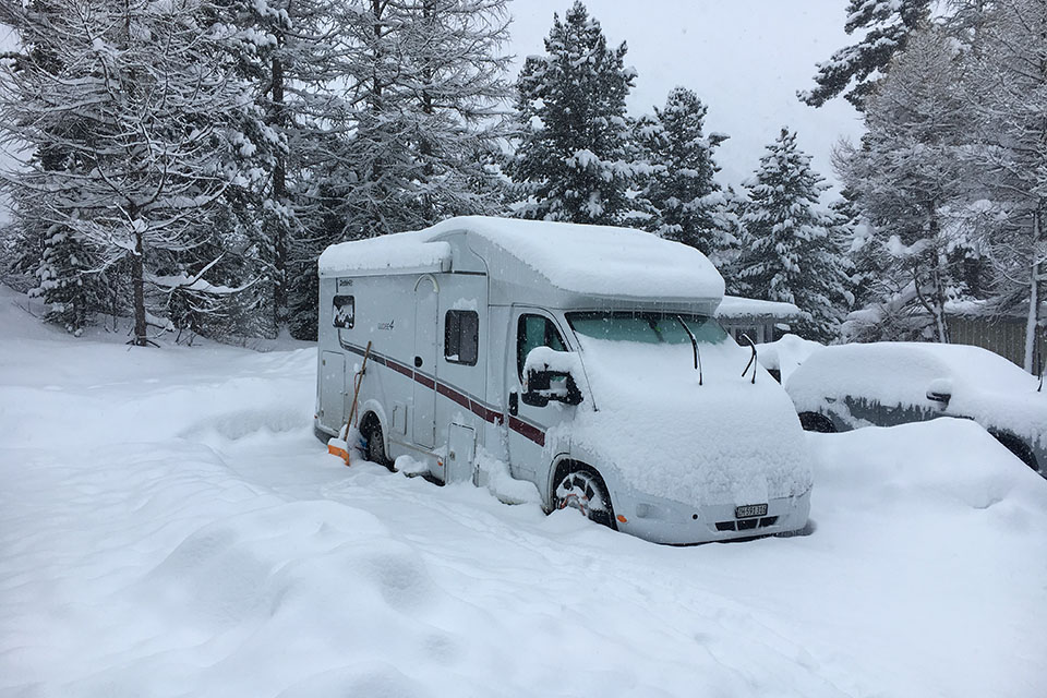 Eingeschneites Wohnmobil auf dem Campingplatz Morteratsch bei starkem Schneefall, Schneeschaufel angelehnt